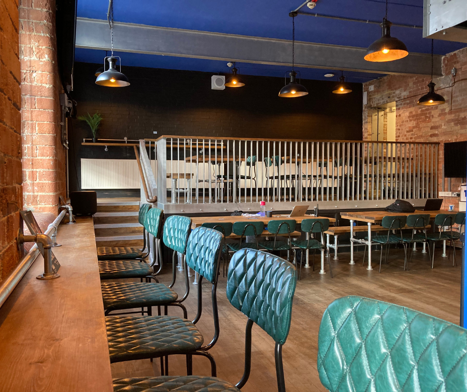 Cafe and bar area at Collective Theatre. With leather green seats and a dark wooden floor and blue ceiling, the space is modern and relaxed.
